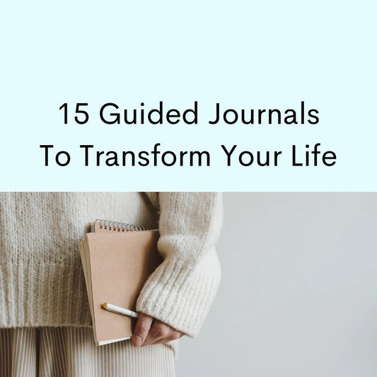 Woman's hand holding tan journal, white pencil. Woman wearing cozy sweater.