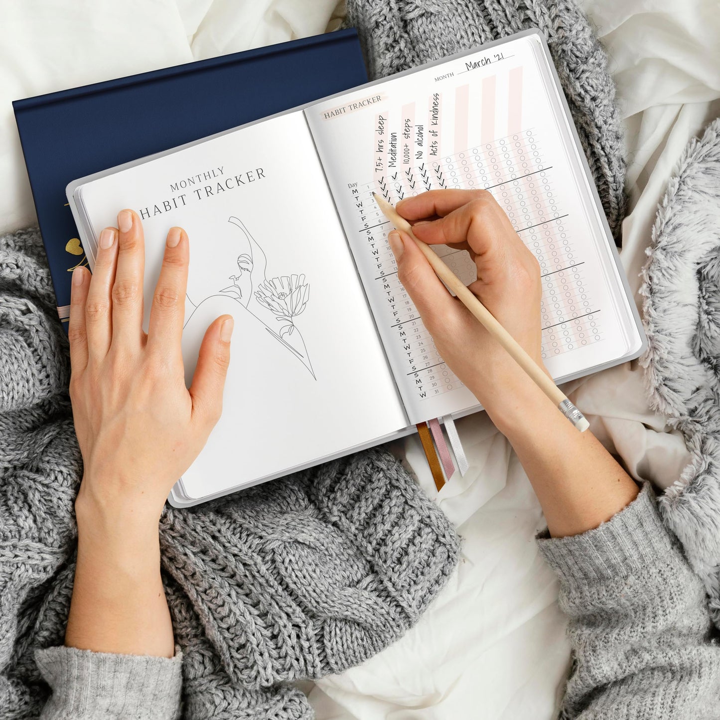 Woman’s hands writing in a journal. Grey knit blanket underneath journal.