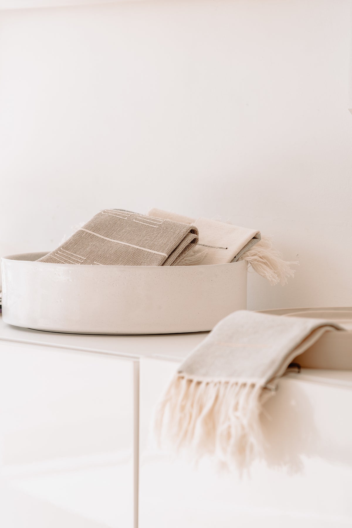 Neutral, minimalist, beige, off white blankets with fringe and stripes in a white basket.